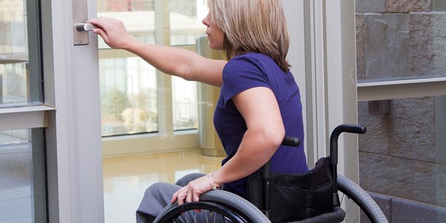 En person som sitter i rullstol och som öppnar en dörr. Foto