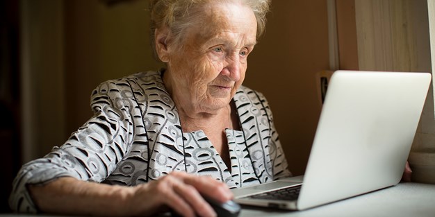En äldre kvinna använder en dator. Foto