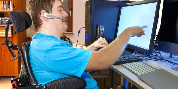 En rullstolsburen person som arbetar vid en dator. Foto