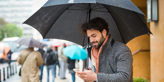 En person på en regnig gata med paraply och smartphone i sina händer. Foto