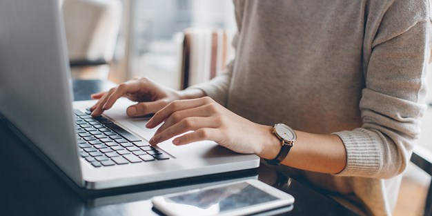 A person using a laptop and a smartphone. Photo