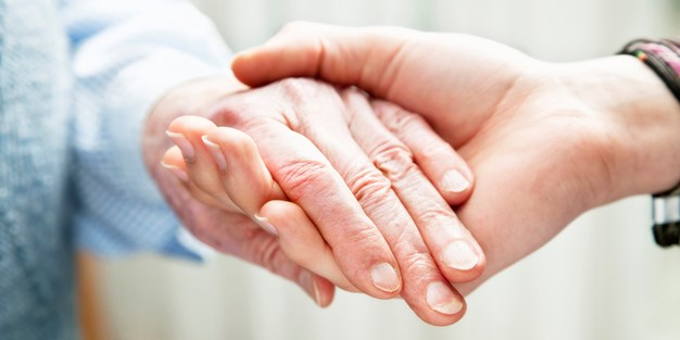 En äldre hand som håller i en yngre människas hand. Foto