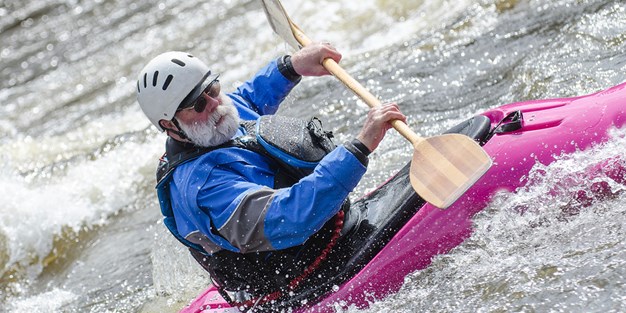 An older man kayaking in a rapid. Photograph