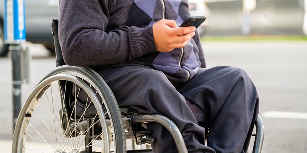 En person i rullstol som använder en smartphone. Foto