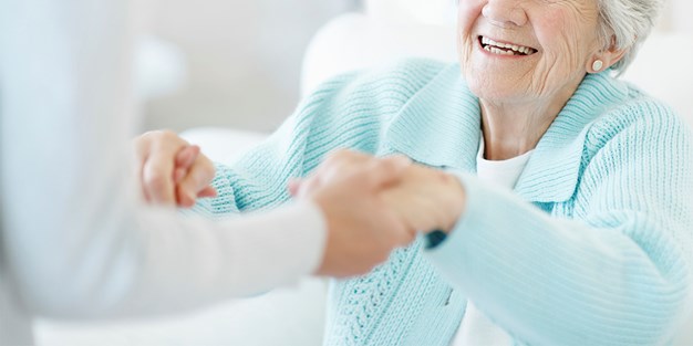 Äldre kvinna i ljusblå tröjan får hjälp att resa sig. Foto