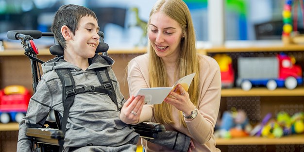 A teacher reading for a student in a wheelchair, photo.