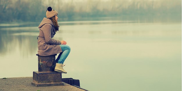 Young girl sitting on a pier looking out over the water. Photo