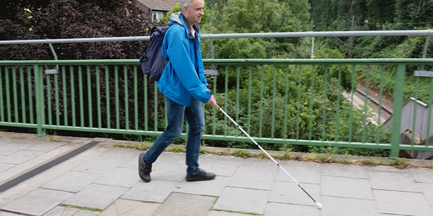 En synskadad person som går med en vit käpp. Foto